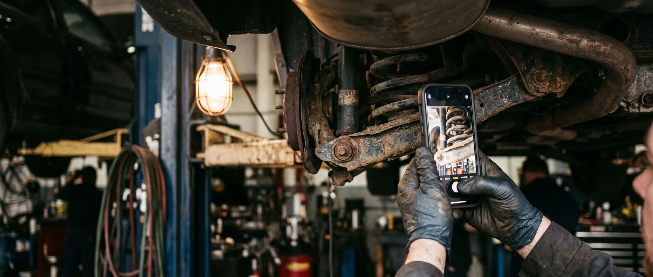 A technician photographing a worn suspension component under a raised car