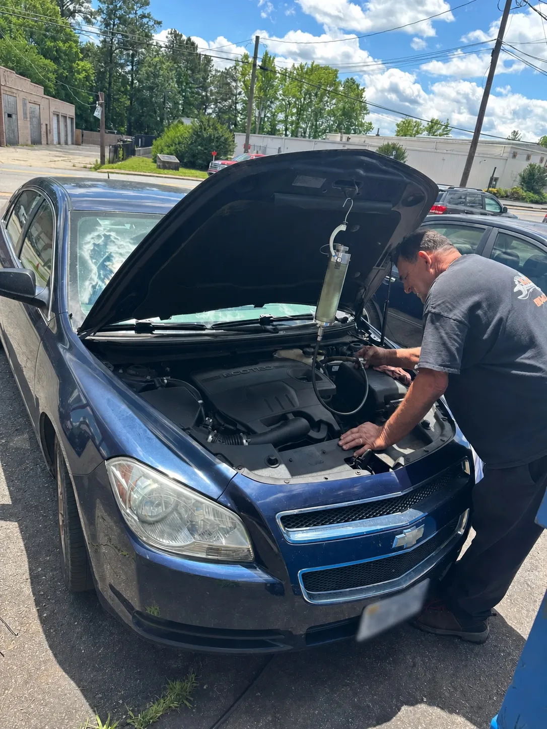 A Lloyd’s technician working under the hood of a blue Chevrolet outside the shop